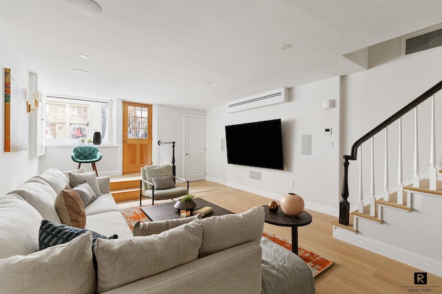 living area featuring baseboards, visible vents, light wood finished floors, stairs, and an AC wall unit