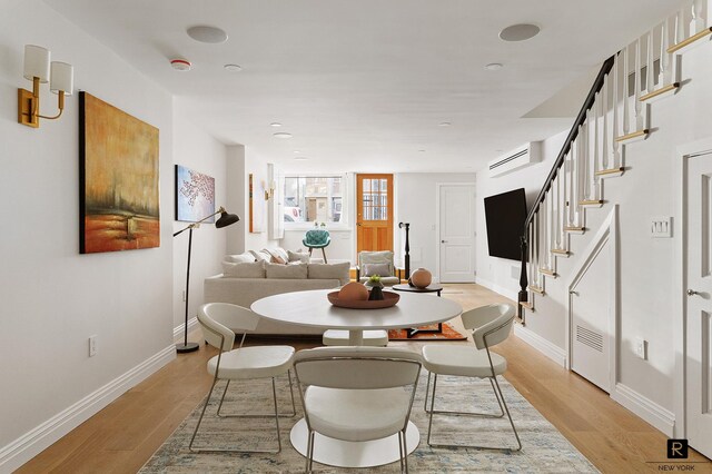 dining room featuring baseboards, stairs, a wall unit AC, and light wood-type flooring