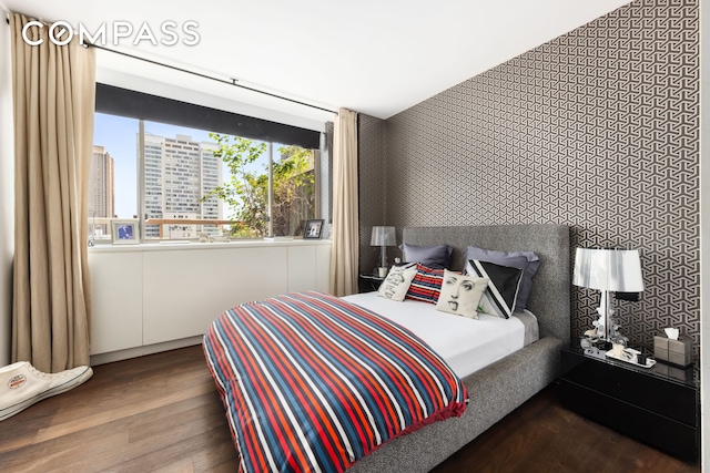 bedroom with wallpapered walls, a view of city, and wood finished floors