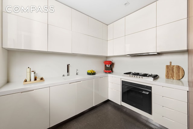 kitchen with stainless steel gas cooktop, light countertops, white cabinets, a sink, and oven