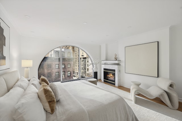 bedroom with baseboards, a premium fireplace, light wood-type flooring, and crown molding