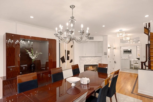 dining room with wood-type flooring, a stone fireplace, crown molding, and a chandelier