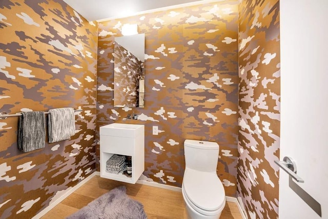 bathroom with toilet, baseboards, wallpapered walls, wood finished floors, and vanity