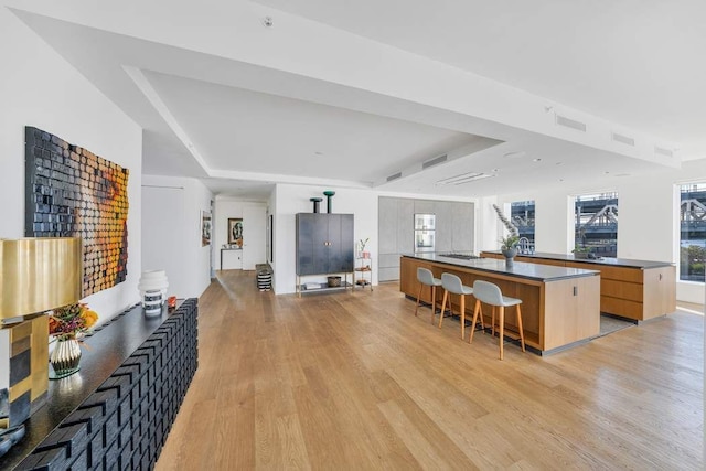 kitchen with a breakfast bar, a kitchen island with sink, light hardwood / wood-style floors, a raised ceiling, and light brown cabinets