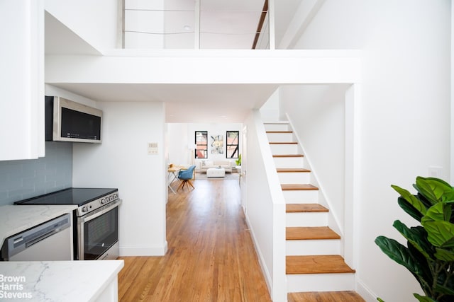 kitchen featuring light stone counters, stainless steel appliances, light wood-type flooring, and backsplash