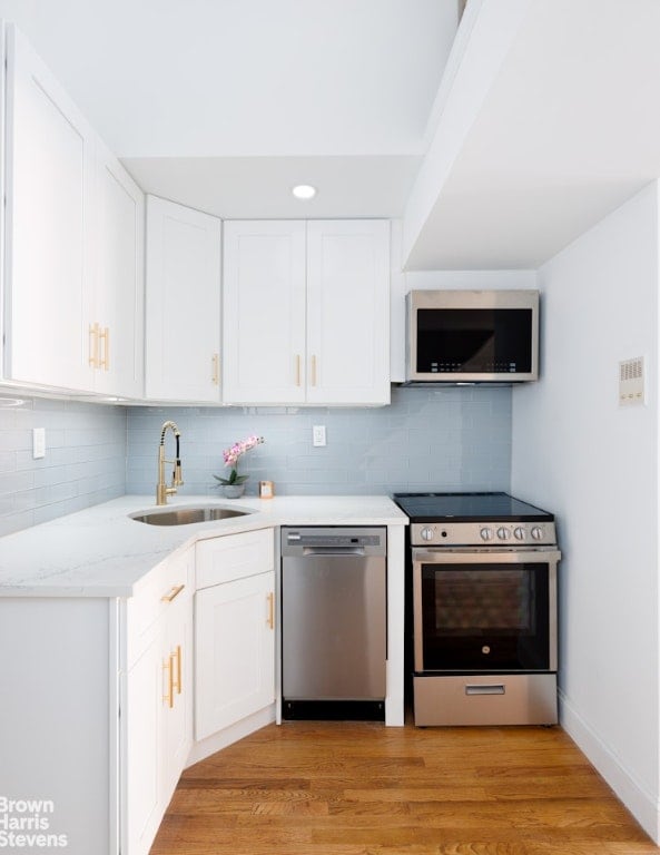 kitchen with light wood-type flooring, appliances with stainless steel finishes, sink, and white cabinets