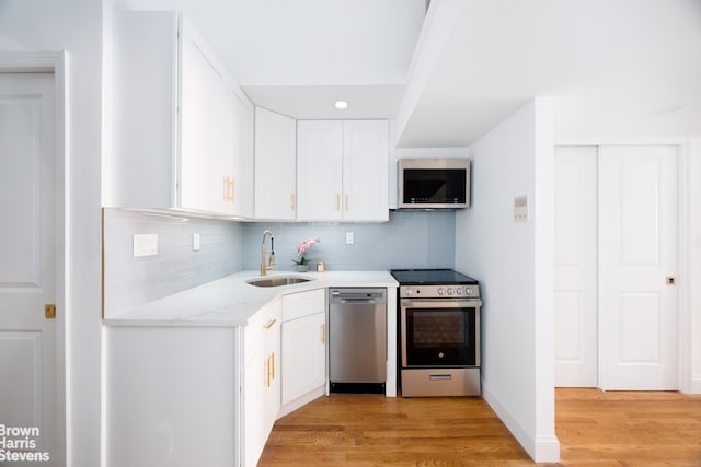 kitchen with stainless steel appliances, sink, white cabinets, and light wood-type flooring