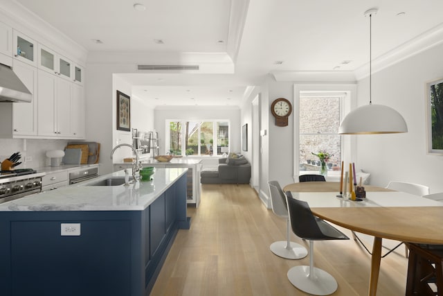 kitchen with a sink, visible vents, light wood finished floors, an island with sink, and crown molding