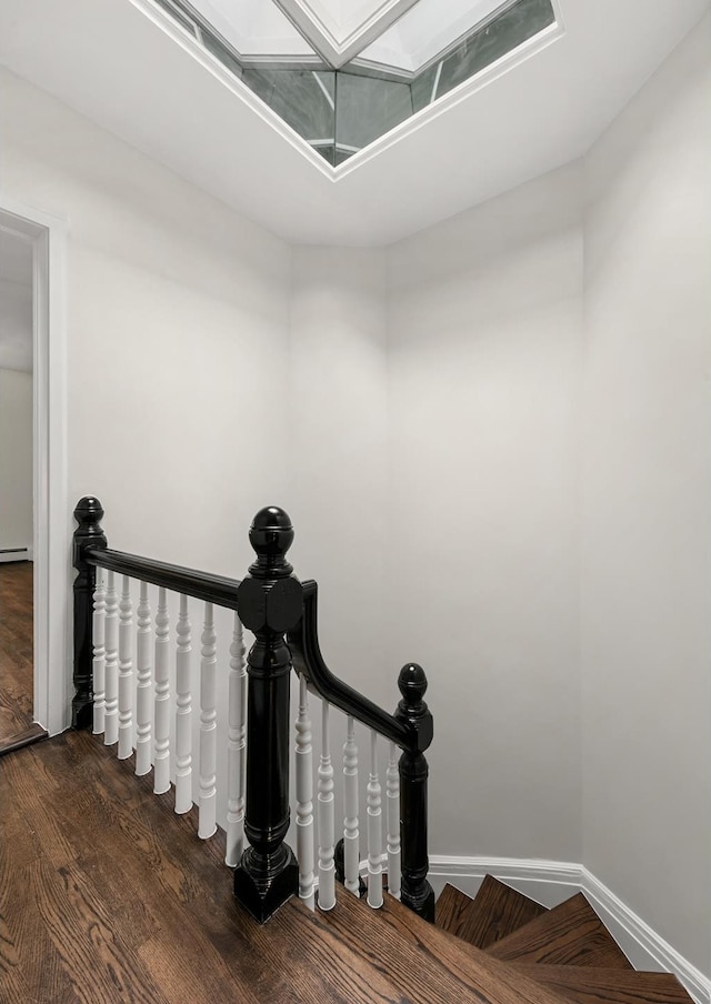 staircase featuring a skylight, wood finished floors, and baseboards