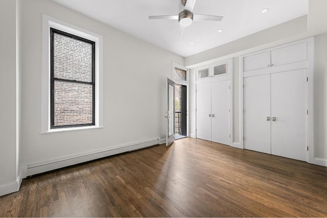 unfurnished bedroom featuring ceiling fan, a baseboard heating unit, dark hardwood / wood-style flooring, and two closets