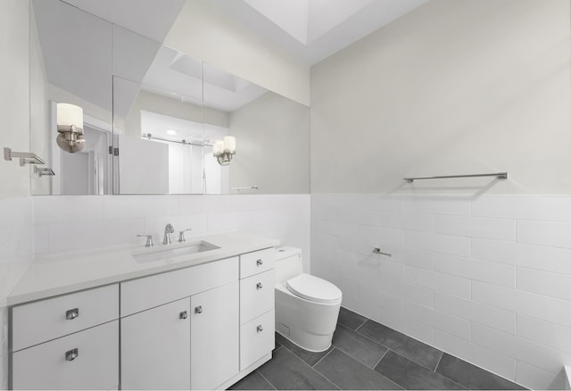 bathroom featuring tile patterned floors, a wainscoted wall, toilet, tile walls, and vanity