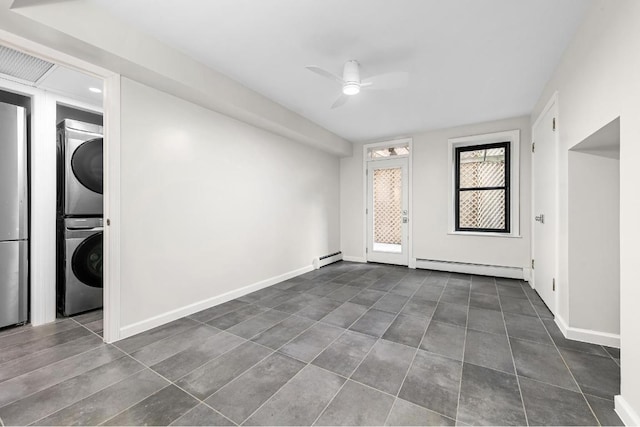 spare room with stacked washing maching and dryer, baseboard heating, and ceiling fan