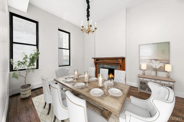 dining area with a chandelier, baseboards, wood finished floors, and a high end fireplace