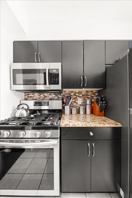 kitchen with stainless steel appliances, tasteful backsplash, light stone countertops, and light tile patterned floors