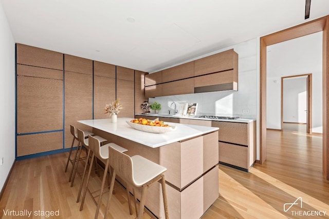 kitchen featuring stainless steel gas cooktop, light hardwood / wood-style flooring, a kitchen breakfast bar, a kitchen island, and backsplash