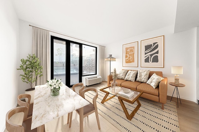 living area featuring baseboards, light wood-style flooring, and a wall unit AC