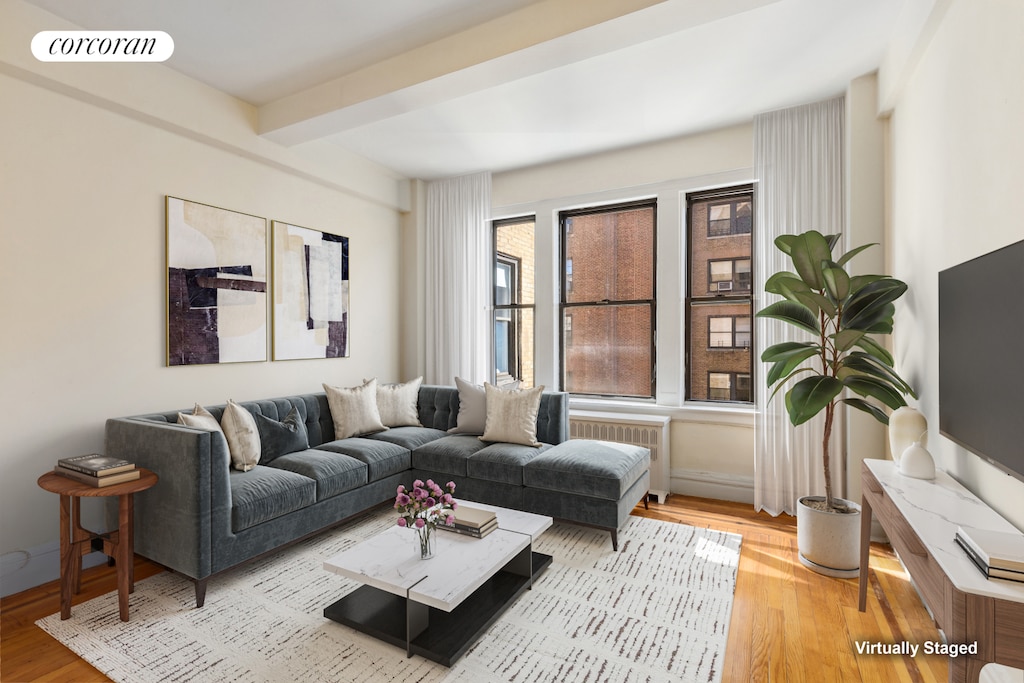 living room featuring beamed ceiling, radiator heating unit, wood finished floors, and visible vents