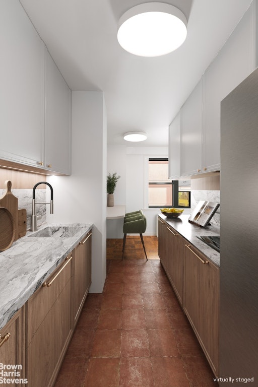 kitchen featuring light stone countertops, white cabinetry, and sink