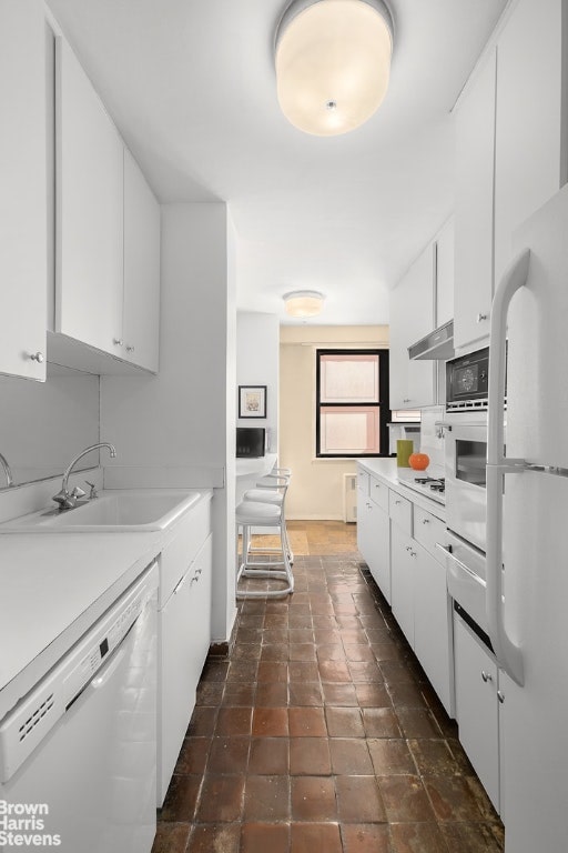 kitchen with white cabinetry, sink, white appliances, and radiator