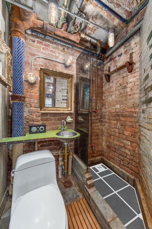 bathroom with toilet, brick ceiling, brick wall, and sink