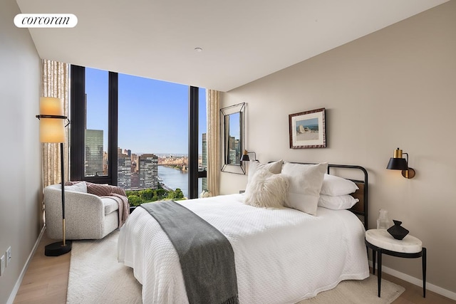 bedroom featuring a water view, wood finished floors, visible vents, baseboards, and a wall of windows