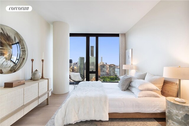 bedroom with visible vents, floor to ceiling windows, a city view, and wood finished floors