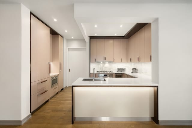 kitchen with light countertops, decorative backsplash, light wood-style floors, a sink, and a peninsula