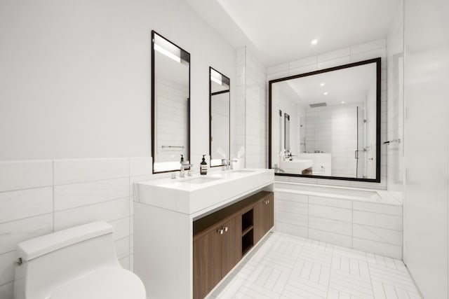 bathroom featuring double vanity, tile walls, tiled shower, toilet, and a sink