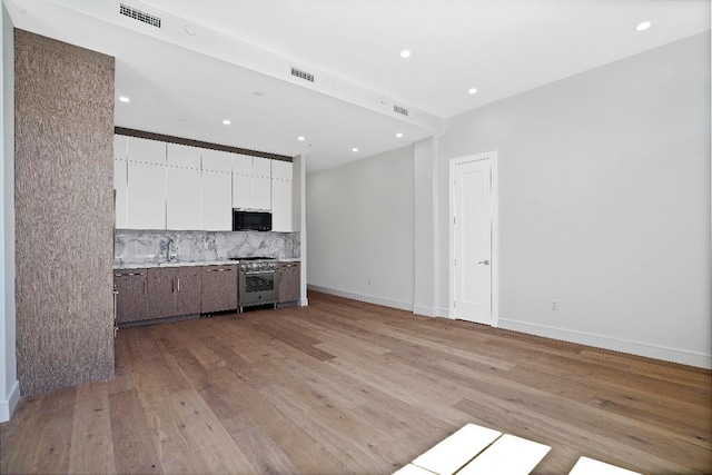 kitchen featuring backsplash, white cabinetry, light hardwood / wood-style flooring, high end stainless steel range, and dark brown cabinets