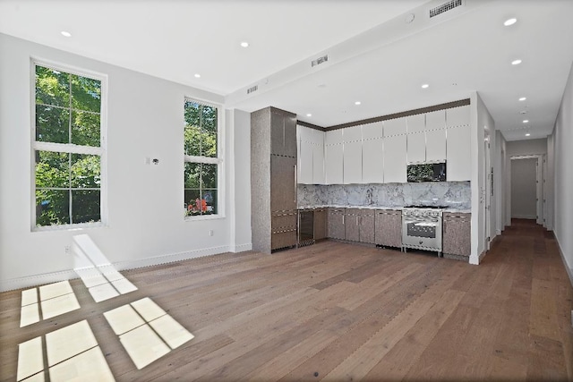 kitchen featuring backsplash, sink, white cabinetry, light wood-type flooring, and stainless steel range