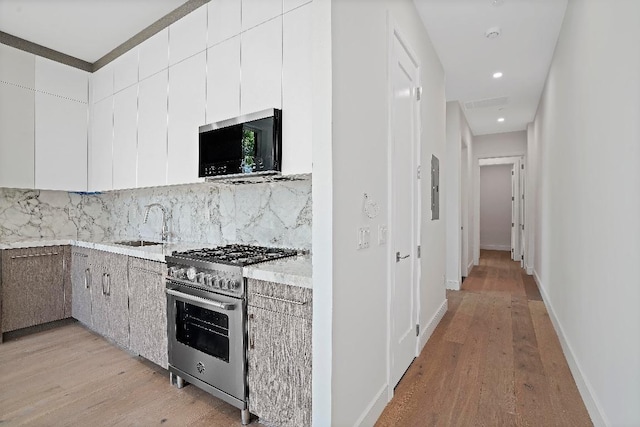 kitchen featuring high end range, white cabinetry, decorative backsplash, sink, and light wood-type flooring