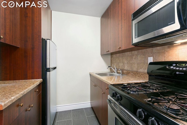 kitchen with sink, light stone counters, tasteful backsplash, appliances with stainless steel finishes, and dark tile patterned flooring