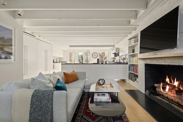 living room with a brick fireplace, beamed ceiling, and light wood-type flooring