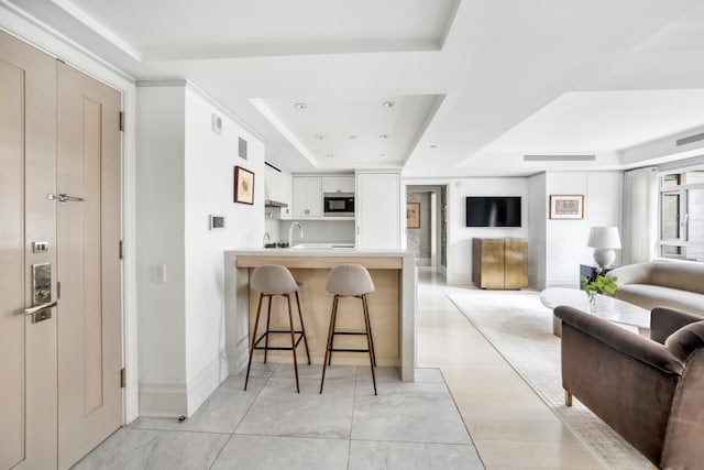 kitchen with a breakfast bar, stainless steel microwave, white cabinets, kitchen peninsula, and a raised ceiling