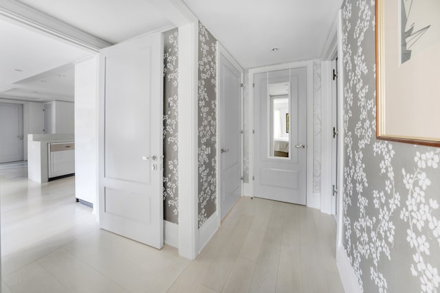 hall featuring wallpapered walls, baseboards, and light wood-type flooring