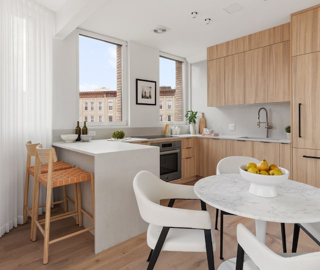 kitchen featuring light hardwood / wood-style floors, kitchen peninsula, light brown cabinets, oven, and sink