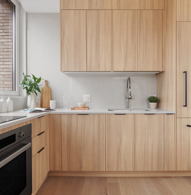 kitchen featuring stainless steel oven, black electric cooktop, light wood-type flooring, light brown cabinetry, and sink