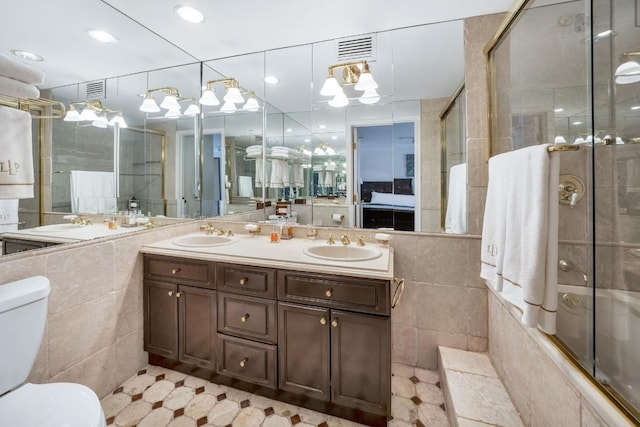 full bathroom featuring tile walls, enclosed tub / shower combo, vanity, and toilet