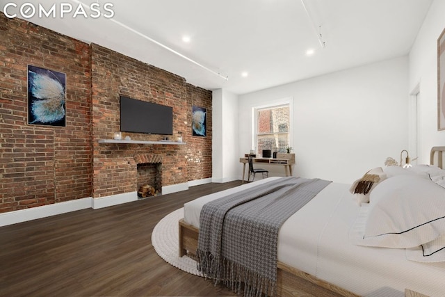 bedroom featuring dark wood-type flooring, brick wall, and a fireplace