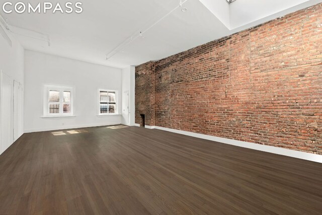 empty room featuring brick wall and dark hardwood / wood-style floors