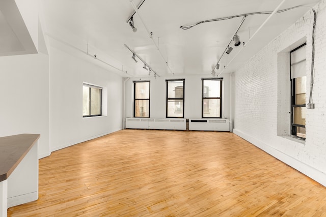 unfurnished living room with brick wall, rail lighting, and light hardwood / wood-style flooring