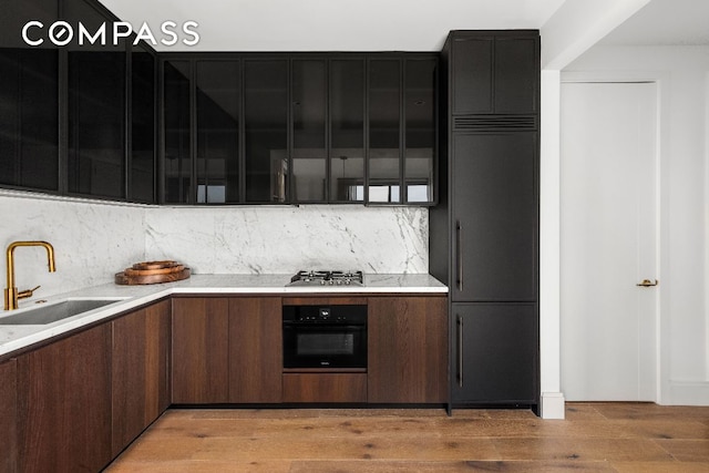 kitchen with stainless steel gas cooktop, decorative backsplash, sink, light wood-type flooring, and oven