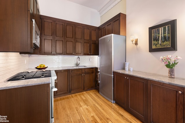 kitchen featuring light stone countertops, stainless steel appliances, a sink, light wood-type flooring, and decorative backsplash