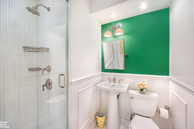 bathroom featuring wainscoting, a shower stall, toilet, and a decorative wall