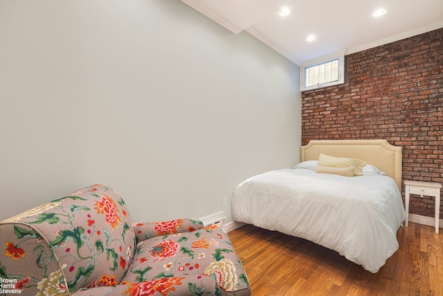 bedroom featuring lofted ceiling, ornamental molding, brick wall, wood finished floors, and baseboards