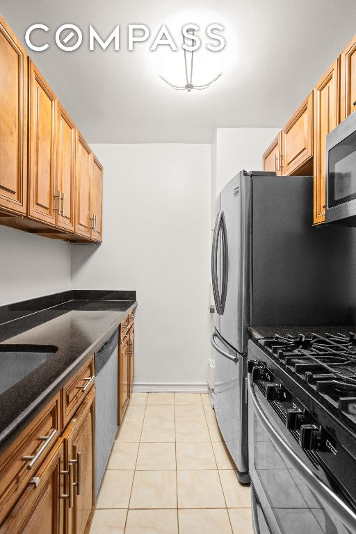 kitchen with stainless steel appliances, light tile patterned floors, and dark stone counters