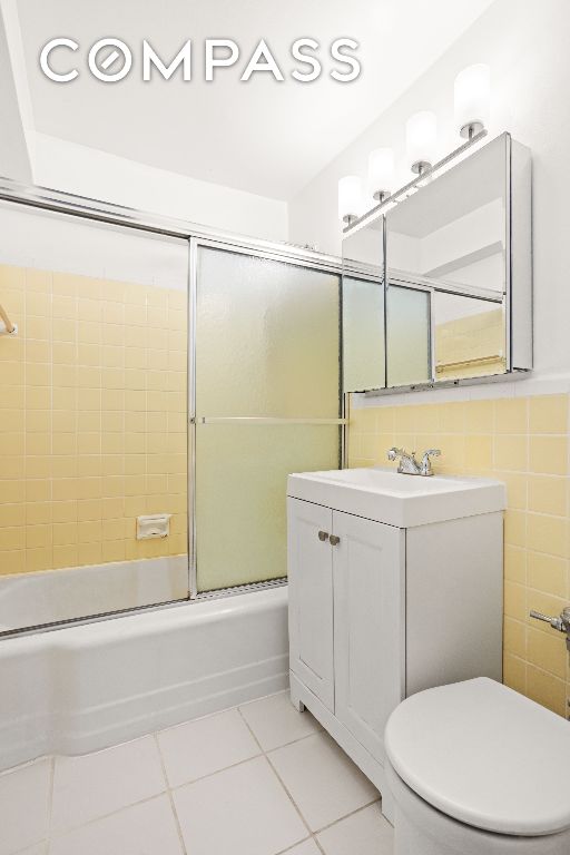 full bathroom featuring shower / bath combination with glass door, tile walls, vanity, tile patterned floors, and toilet