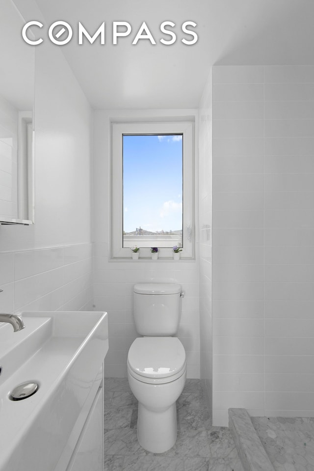 bathroom featuring tile walls, toilet, tiled shower, marble finish floor, and vanity