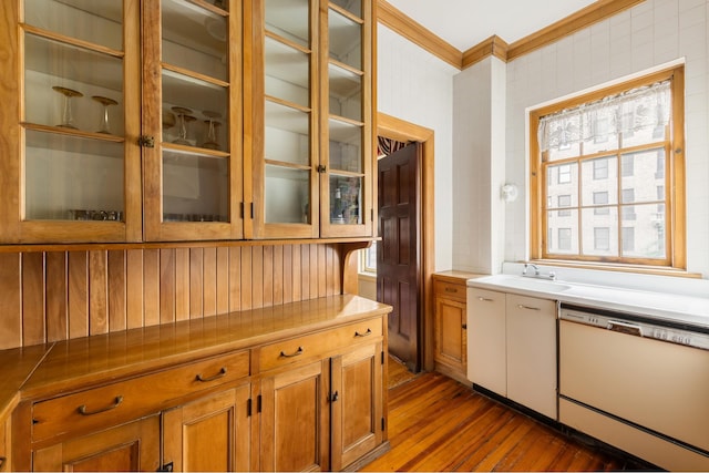 kitchen featuring glass insert cabinets, crown molding, brown cabinets, dishwasher, and hardwood / wood-style flooring