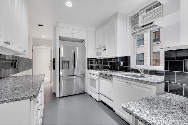 kitchen with stone countertops, white appliances, white cabinets, backsplash, and sink